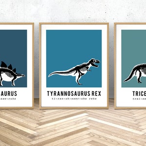 May include: Three framed prints of dinosaur skeletons with their names and phonetic pronunciations below. The prints are on a blue background with a wooden frame.