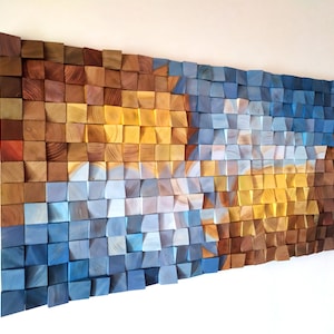 Op de afbeelding: Een wandkunstwerk gemaakt van houten blokken in tinten blauw, bruin en geel. De blokken zijn gerangschikt in een geometrisch patroon, waardoor een textuurrijk en abstract ontwerp ontstaat.