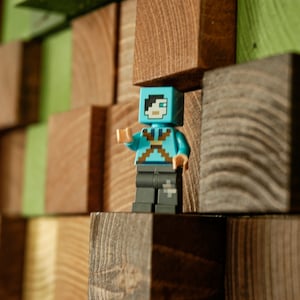 Op de afbeelding: Een blauwe en zwarte Lego minifiguur staat op een houten plank gemaakt van verschillende houttinten. De minifiguur draagt een blauw shirt met een wit kruis en een zwarte broek.