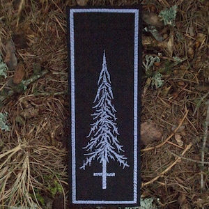 Può includere: Toppa rettangolare nera con un design ad albero bianco stilizzato e una croce alla base. L'albero ha rami dettagliati e una cima appuntita. La toppa è bordata da una sottile linea bianca.