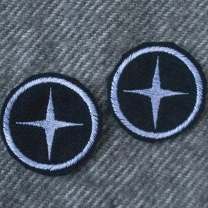 Pode incluir: Dois patches bordados em preto e branco com um design de estrela branca. Os patches são circulares e têm uma borda branca.