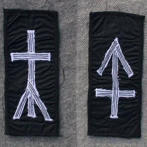 May include: Two black fabric patches with white embroidered symbols. The patch on the left has a cross with a tree-like base. The patch on the right has an arrow with a cross at the base.
