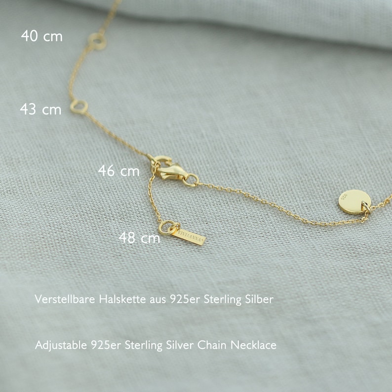 May include: A gold chain necklace with a small round charm. The necklace is adjustable and measures 40, 43, 46, and 48 cm. The necklace is made of 925 sterling silver.