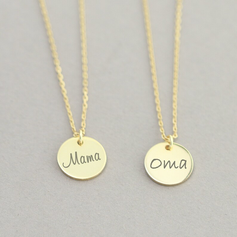 May include: Two gold necklaces with round pendants. The pendant on the left says "Mama" and the pendant on the right says "Oma".