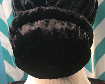 Può includere: Turbante in velluto nero con un design plissettato. Il turbante è indossato sulla testa di un manichino.