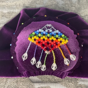 May include: A purple velvet hat with a beaded rainbow design and crystal accents.