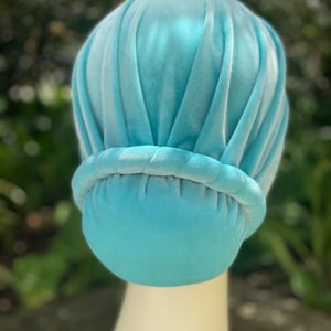 May include: A light blue velvet turban with a gathered top and a smooth, rounded bottom.