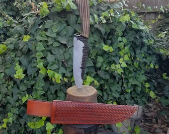 May include: A handmade knife with a wooden handle and a leather sheath. The knife is resting on a wooden stump, and the sheath is wrapped around the stump.