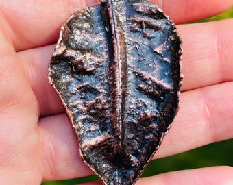 May include: A copper leaf pendant with a textured surface. The pendant has a loop at the top for attaching to a chain.
