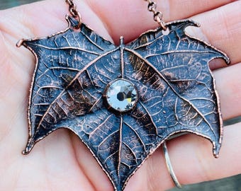 May include: A copper leaf pendant necklace with a clear crystal in the center. The leaves are detailed and textured, giving the piece a rustic look.