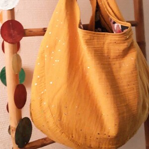 May include: A large, yellow tote bag with a subtle shimmer. The bag has a gathered, loose, and unstructured shape.