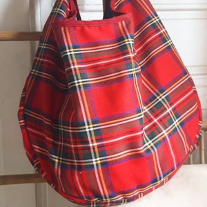 May include: Red and green plaid tote bag with a rounded bottom. The bag is made of a thick fabric and has a simple design.