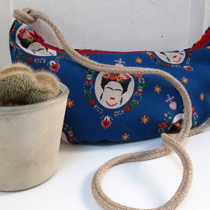 May include: A blue canvas bag with a rope strap. The bag has a repeating pattern of a woman's face with flowers and hearts.