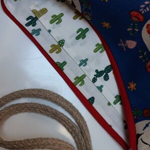 May include: A blue fabric bag with a white lining and a red zipper. The bag has a floral pattern with cacti and a rope strap.