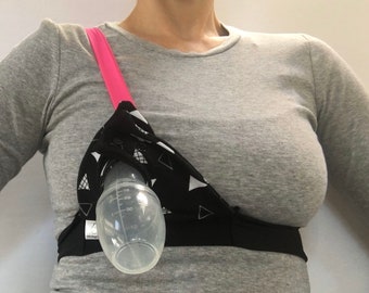 May include: A black and white patterned nursing bra with a pink strap and a clear plastic bottle attached to the front.