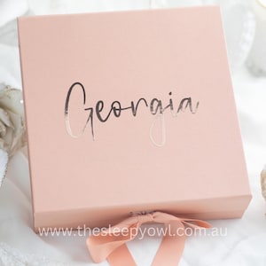 May include: A pale pink gift box with a silver foil inscription that reads "Georgia" and a pink satin ribbon.
