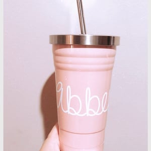 May include: A pink stainless steel tumbler with a white lid and a white straw. The tumbler has the word "abbey" written on it in white.