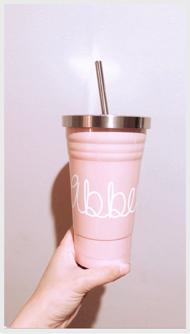 May include: A pink stainless steel tumbler with a white lid and a white straw. The tumbler has the word "abbey" written on it in white.