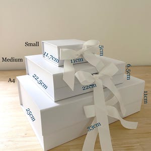 May include: Three white rectangular gift boxes stacked in size order, each featuring a white ribbon bow. The small box measures 11.7cm by 11cm by 5cm, the medium box 22.5cm by 22cm by 6.5cm, and the A4 box 25cm by 33cm by 11cm. Text indicates dimensions.