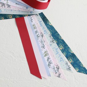 May include: A selection of patterned ribbons in various colours. One is a solid red, others feature zebra and peacock feather designs, and the text "It's a boy!". The ribbons are arranged on a white surface.