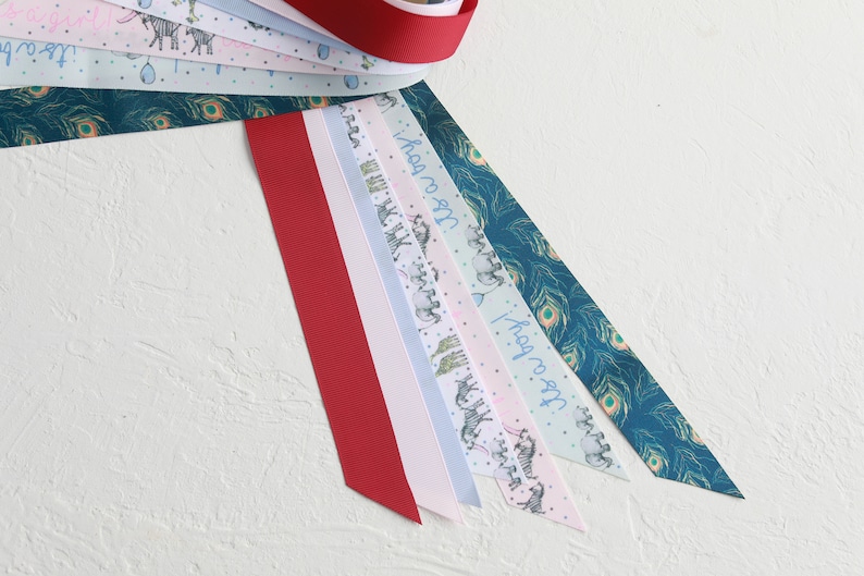 May include: A selection of patterned ribbons in various colours. One is a solid red, others feature zebra and peacock feather designs, and the text "It's a boy!". The ribbons are arranged on a white surface.