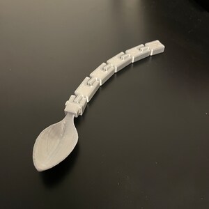 Peut inclure: Une cuillère en plastique grise avec un manche segmenté unique. Le manche est composé de plusieurs pièces connectées, créant un design flexible et intéressant.