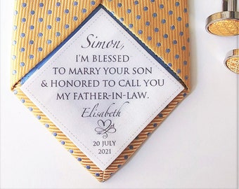 May include: A white tag with a message for a father-in-law, reading "Simon, I'M BLESSED TO MARRY YOUR SON & HONORED TO CALL YOU MY FATHER-IN-LAW. Elisabeth 20 JULY 2021". The tag is attached to a yellow tie with blue polka dots.