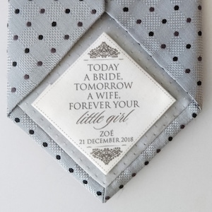 Könnte beinhalten: Eine graue Krawatte mit schwarzen Punkten und einem weißen Etikett. Das Etikett trägt den Text "TODAY A BRIDE, TOMORROW A WIFE, FOREVER YOUR little girl ZOÉ 21 DECEMBER 2018".