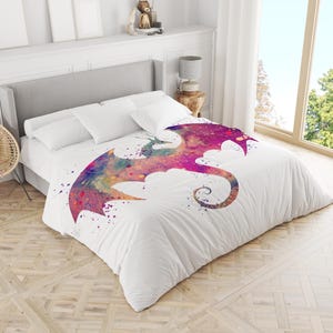 Può includere: Copripiumino bianco con un colorato disegno di drago ad acquerello. Il drago ha un corpo viola, rosa e arancione con una lunga coda arricciata. Il disegno è cosparso di vernice viola e blu.