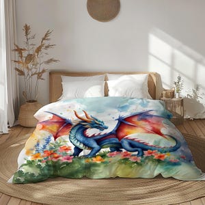 May include: A watercolor-style duvet cover featuring a blue dragon with orange horns and wings. The dragon is set against a backdrop of a watercolor sky and colorful flowers. The bedding is on a bed with white pillows.