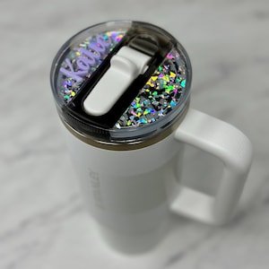 May include: White travel mug with a clear lid featuring a holographic glitter design and a personalized name "Kalie" in purple lettering.