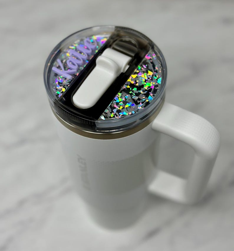 May include: White travel mug with a clear lid featuring a holographic glitter design and a personalized name "Kalie" in purple lettering.