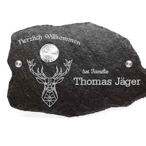 Könnte beinhalten: Schwarzes Schiefer-Hausschild mit einem geometrischen Hirsch-Design, dem Text "Herzlich Willkommen bei Familie Thomas Jäger" und einer Türklingel.