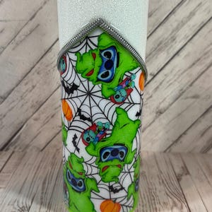 Pu&ograve; includere: Un bicchiere bianco glitterato con un design a tema Halloween. Il design presenta un personaggio verde con occhi blu, pipistrelli, ragnatele e zucche arancioni. Un bordo argentato accentua la parte superiore del design.