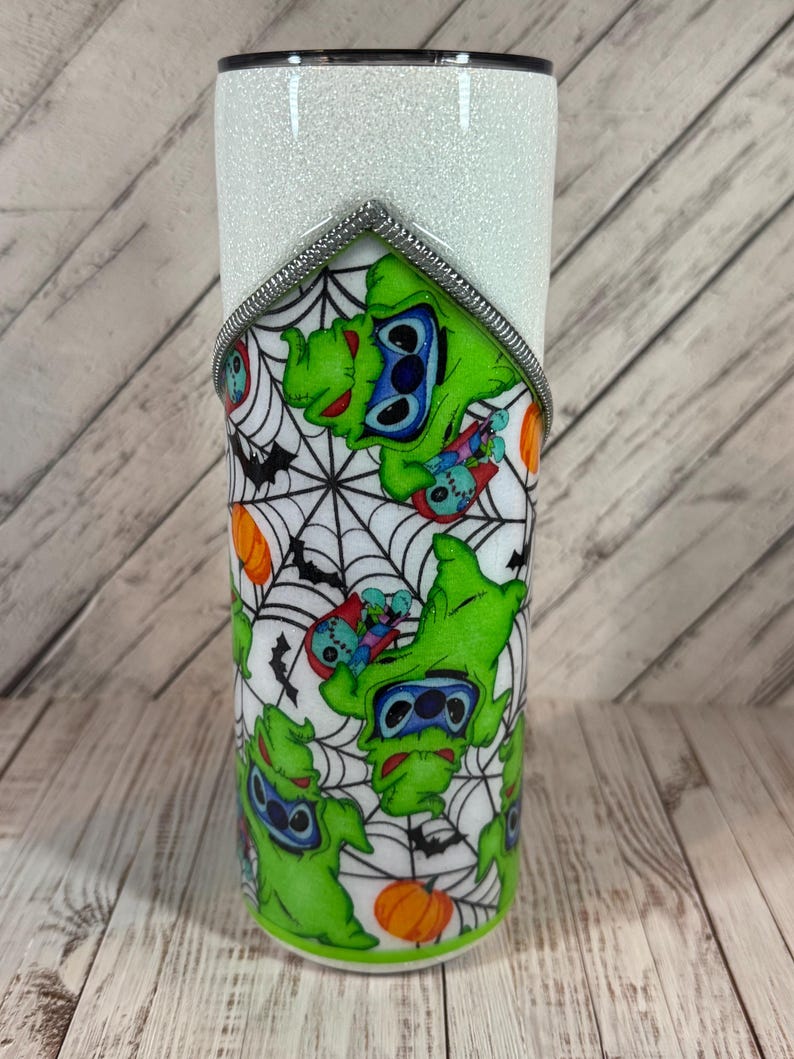 Pu&ograve; includere: Un bicchiere bianco glitterato con un design a tema Halloween. Il design presenta un personaggio verde con occhi blu, pipistrelli, ragnatele e zucche arancioni. Un bordo argentato accentua la parte superiore del design.