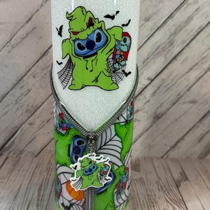 Pu&ograve; includere: Un bicchiere bianco glitterato con un personaggio dei cartoni animati in costume verde e un design a cerniera. Il bicchiere ha un coperchio nero e un design verde e bianco abbinato con ragnatele e pipistrelli. Un ciondolo del personaggio pende dalla cerniera.
