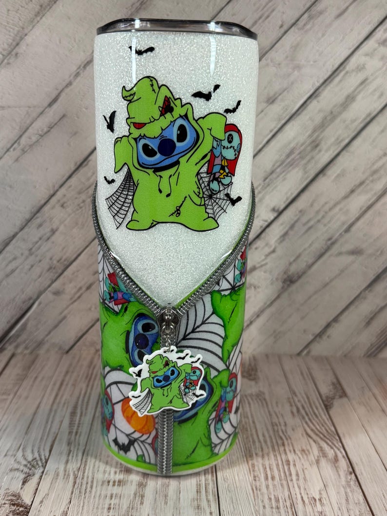 Pu&ograve; includere: Un bicchiere bianco glitterato con un personaggio dei cartoni animati in costume verde e un design a cerniera. Il bicchiere ha un coperchio nero e un design verde e bianco abbinato con ragnatele e pipistrelli. Un ciondolo del personaggio pende dalla cerniera.