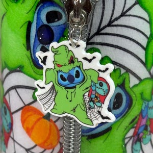 Pu&ograve; includere: Primo piano di un tirazip a tema Halloween con un personaggio dei cartoni animati in costume verde, con un viso blu e che tiene in mano una bambola. Lo sfondo &egrave; un motivo verde e bianco con ragnatele e una zucca.