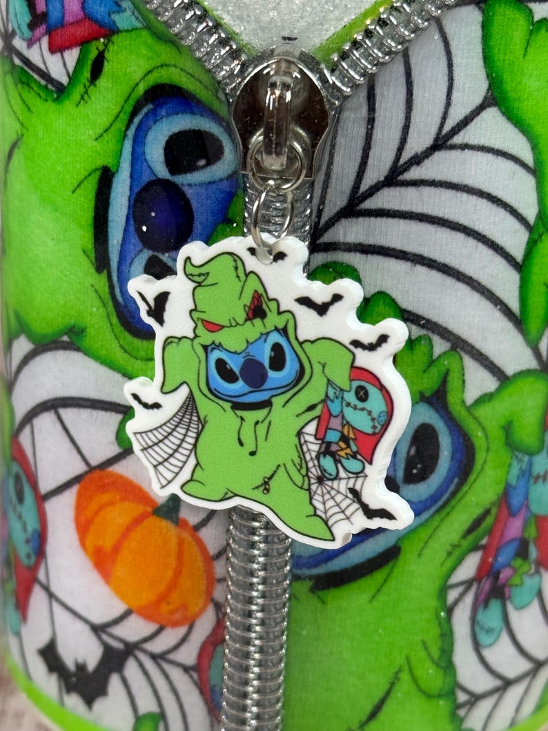 Pu&ograve; includere: Primo piano di un tirazip a tema Halloween con un personaggio dei cartoni animati in costume verde, con un viso blu e che tiene in mano una bambola. Lo sfondo &egrave; un motivo verde e bianco con ragnatele e una zucca.