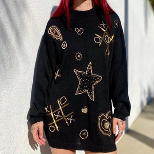 May include: Black sweater with gold sequin embellishments in the shape of hearts, stars, and a tic-tac-toe board.