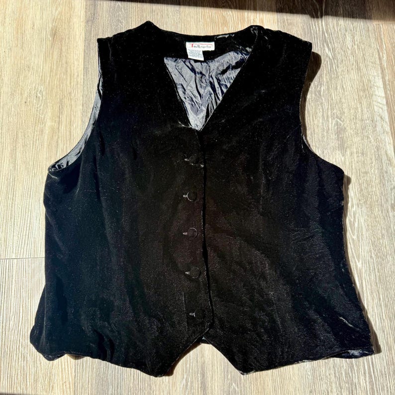 May include: A black velvet vest with a V-neck and button-up closure. The vest has a tailored fit and a satin lining. The garment is a classic piece of apparel.