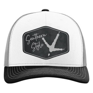 May include: A trucker hat with a white front panel and a gray mesh back. The front features a black and gray hexagon with the words "Southern Style" and a turkey footprint design.