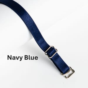 May include: An adjustable strap in navy blue with silver metal hardware. The strap has two loops and a hook.