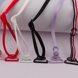 Puede incluir: Variedad de tirantes de sujetador coloridos en varios colores, incluyendo azul claro, rojo, blanco, negro, lavanda y rosa. Cada tirante tiene un gancho y un ajustador de plástico a juego. Un tirante presenta rayas rojas, blancas y azules.