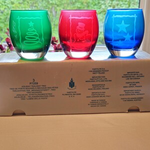 Peut inclure: Un trio de photophores en verre vert, rouge et bleu. Chaque photophore présente un motif gravé festif : un sapin de Noël, un bonhomme de neige et des étoiles. Ensemble de bougies chauffe-plat de Noël.