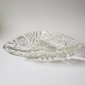 May include: A clear glass serving dish with an elongated, triangular shape. It has detailed etched patterns, including swirling and floral designs. The edges are gently scalloped. This decorative dish is suitable for serving snacks or displaying decorative items. The dish is approximately 30 cm long.
