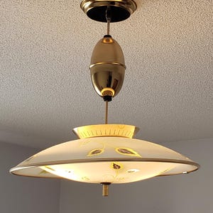 May include: A vintage pendant light fitting with brass and glass elements. It features a circular ceiling rose, a brass body, and a wide, shallow glass shade adorned with leaf patterns. The light hangs from the ceiling.