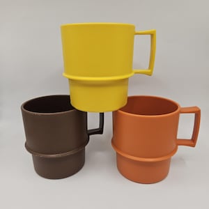 May include: Three brightly coloured plastic mugs stacked together. The top mug is yellow, the middle one is brown, and the bottom one is orange. Each mug has a handle and a unique design, ideal for drinks.