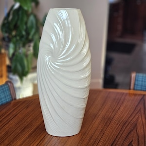 Peut inclure: Un vase en céramique blanc cassé avec un motif en spirale. Le vase a une finition brillante et une base large, se rétrécissant vers le haut. Le motif en spirale crée une surface texturée. Un élément de décoration intérieure.