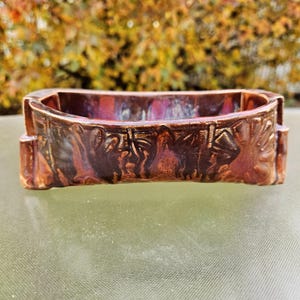 May include: A rectangular ceramic dish with a dark brown, glossy finish. The dish has a raised, textured design on the sides, with a slightly curved interior. The colour transitions from a deep brown to a reddish-purple hue.